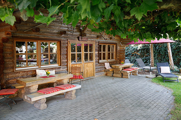 Naturholz-Blockhaus mit Grill und Pizzaofen sowie gepolsterten Gartenmöbeln